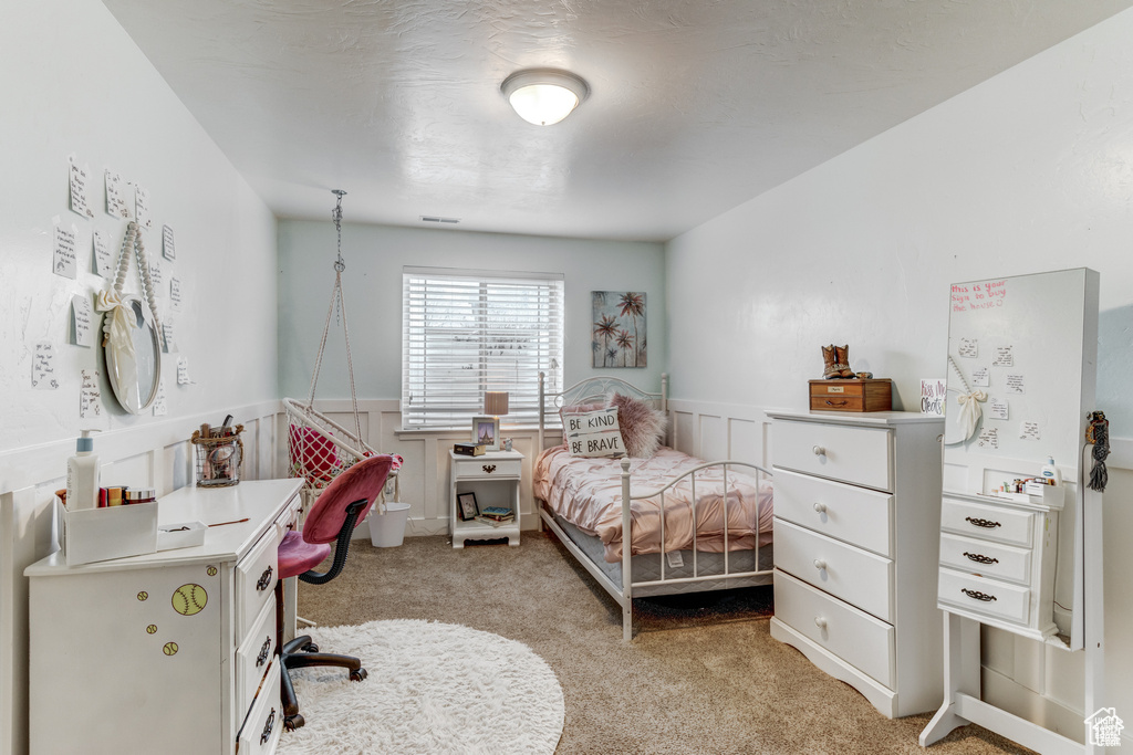 Bedroom with light carpet, wainscoting, and a decorative wall