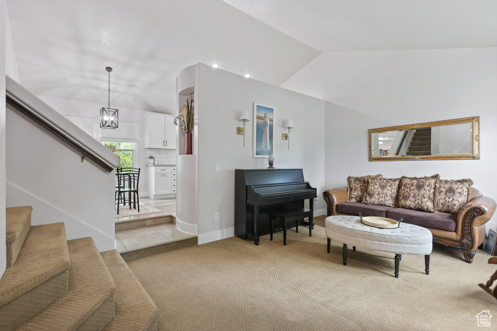 Living area with stairs, light carpet, vaulted ceiling, and baseboards