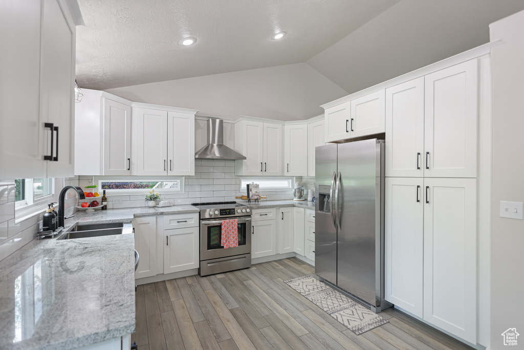 Kitchen with stainless steel appliances, wall chimney exhaust hood, a sink, lofted ceiling, and backsplash