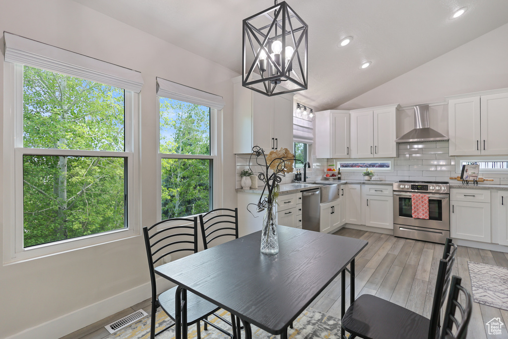 Kitchen featuring stainless steel appliances, wall chimney exhaust hood, decorative backsplash, healthy amount of natural light, and lofted ceiling