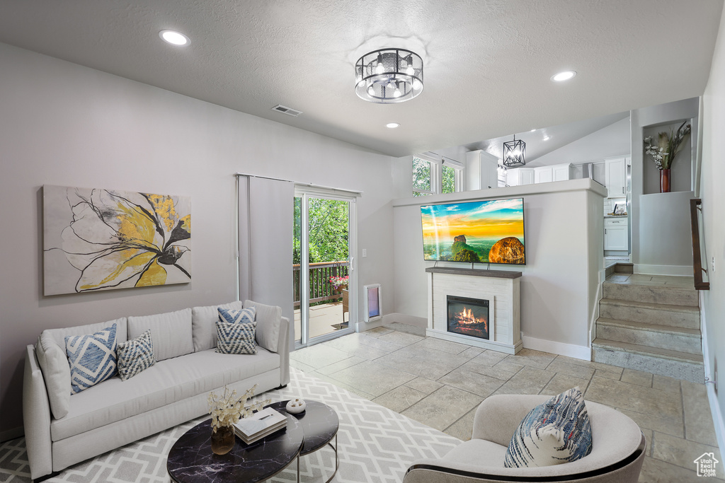 Living room with a chandelier, recessed lighting, a glass covered fireplace, stairs, and a textured ceiling