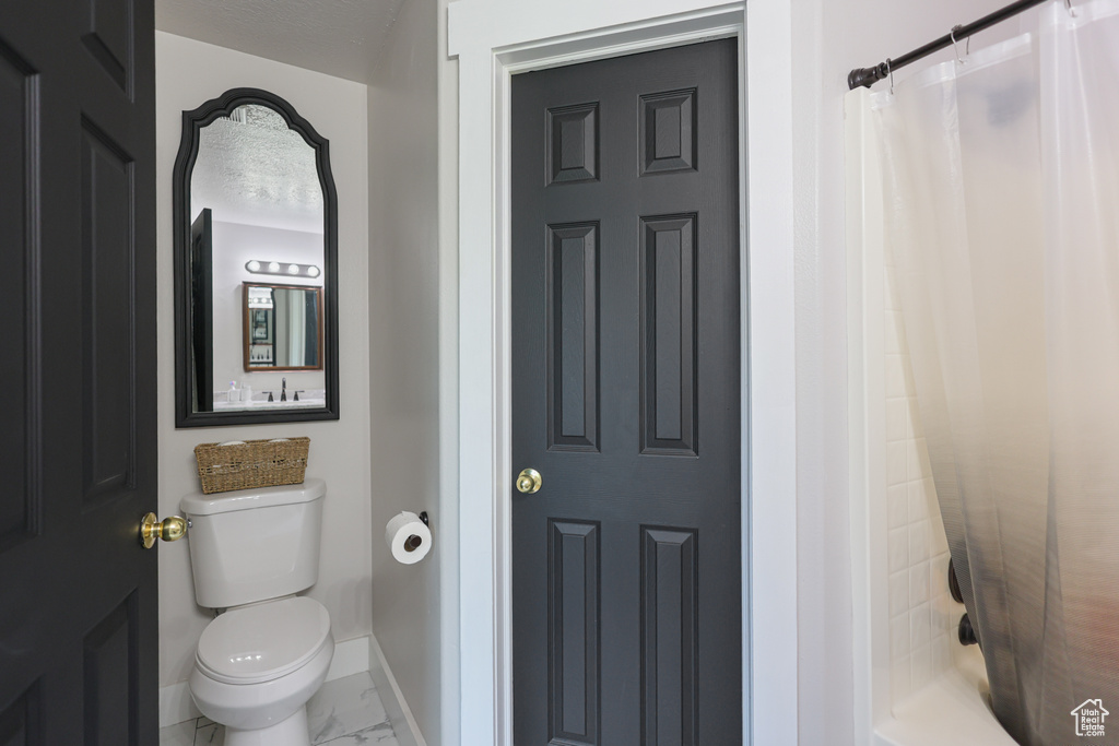 Bathroom with marble finish floors, baseboards, toilet, and shower / tub combo with curtain