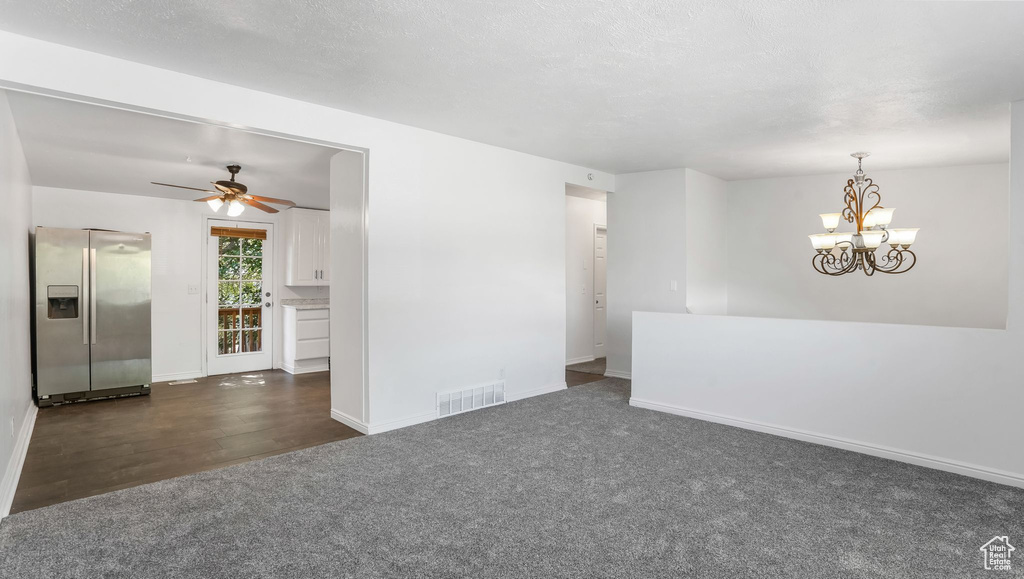 Unfurnished room featuring dark colored carpet, ceiling fan, a chandelier, and dark wood-type flooring