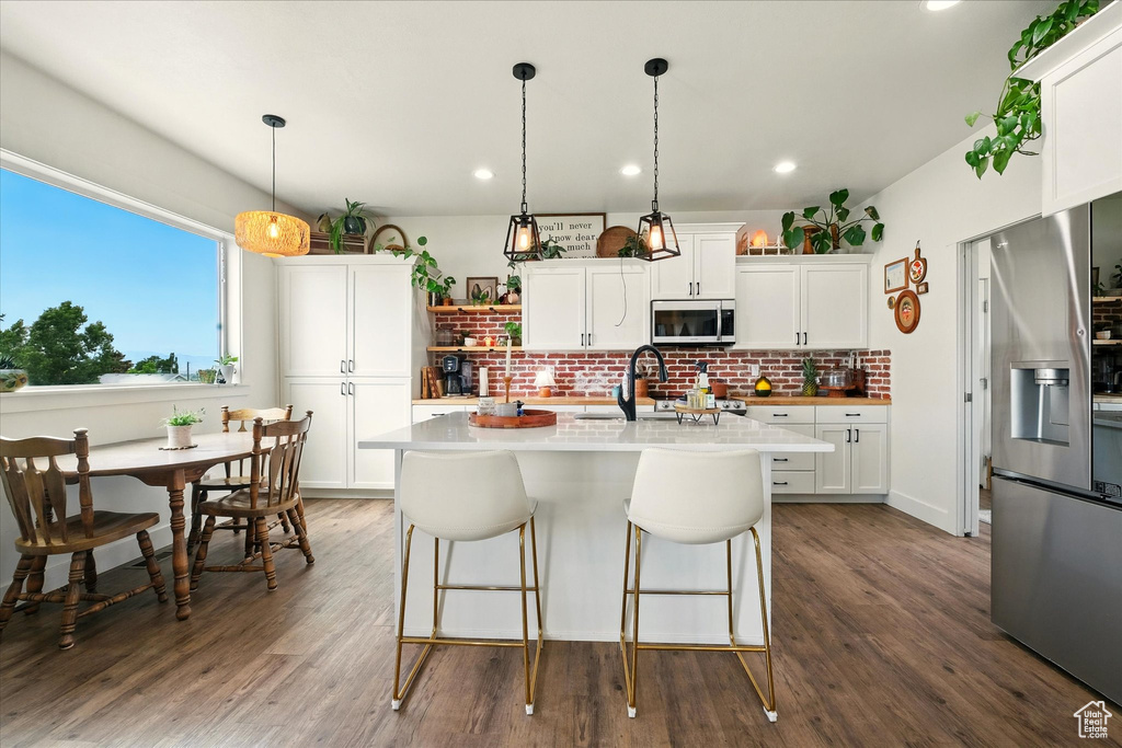 Kitchen featuring appliances with stainless steel finishes, backsplash, light countertops, dark wood-style floors, and an island with sink