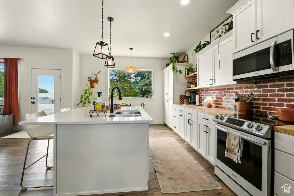 Kitchen with electric stove, plenty of natural light, open shelves, an island with sink, and recessed lighting