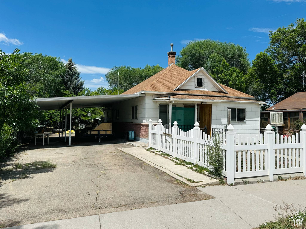 View of front facade with a fenced front yard, a carport, driveway, and roof with shingles