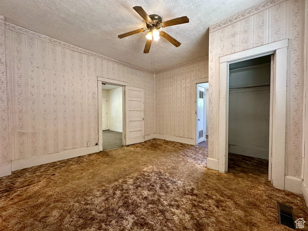 Unfurnished bedroom with carpet flooring, a textured ceiling, a closet, a ceiling fan, and wallpapered walls