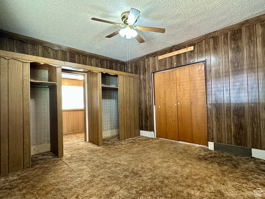 Unfurnished bedroom with wood walls, a textured ceiling, two closets, carpet, and a ceiling fan