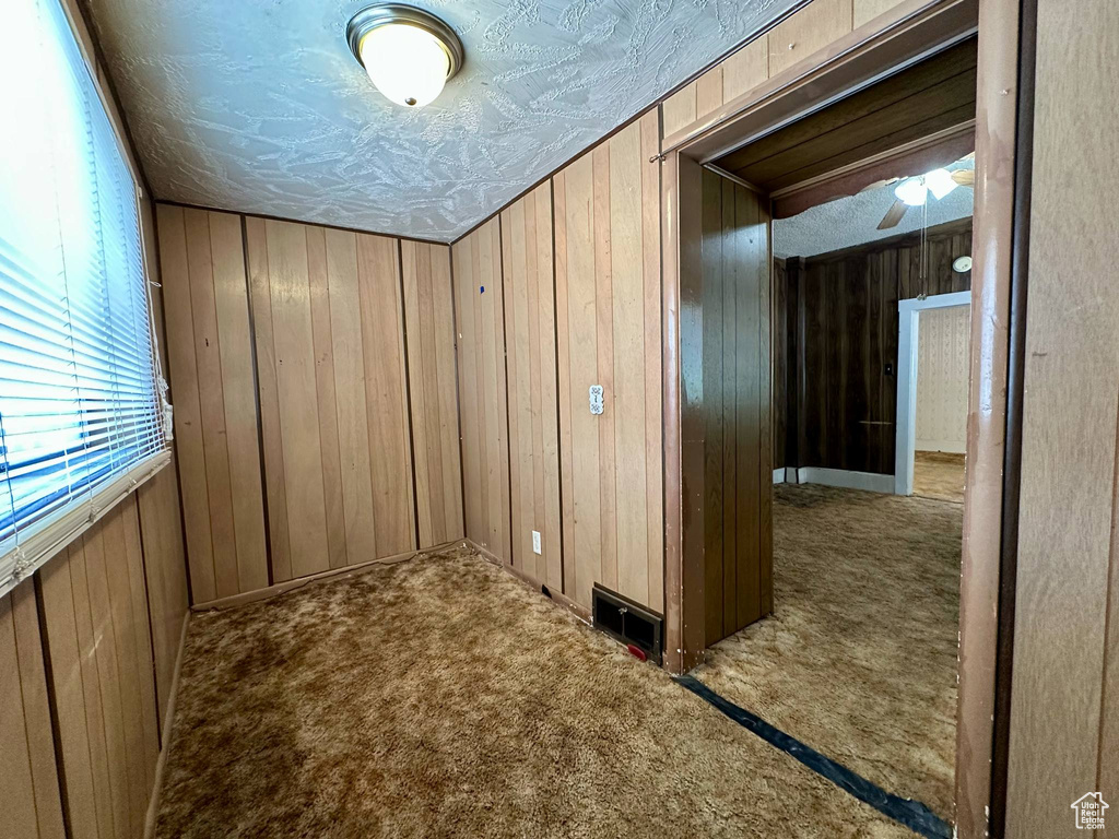 Carpeted spare room with wood walls and a ceiling fan