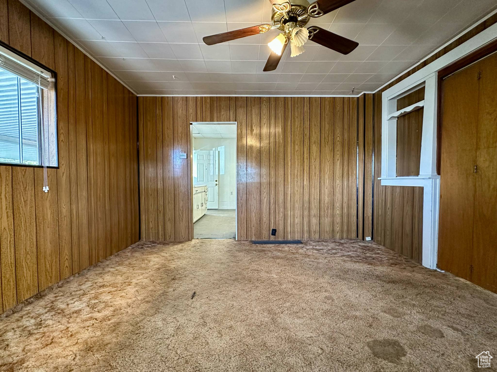 Empty room with carpet flooring, wooden walls, and ceiling fan