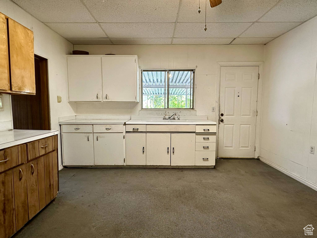 Kitchen with a drop ceiling, light countertops, white cabinetry, and a ceiling fan