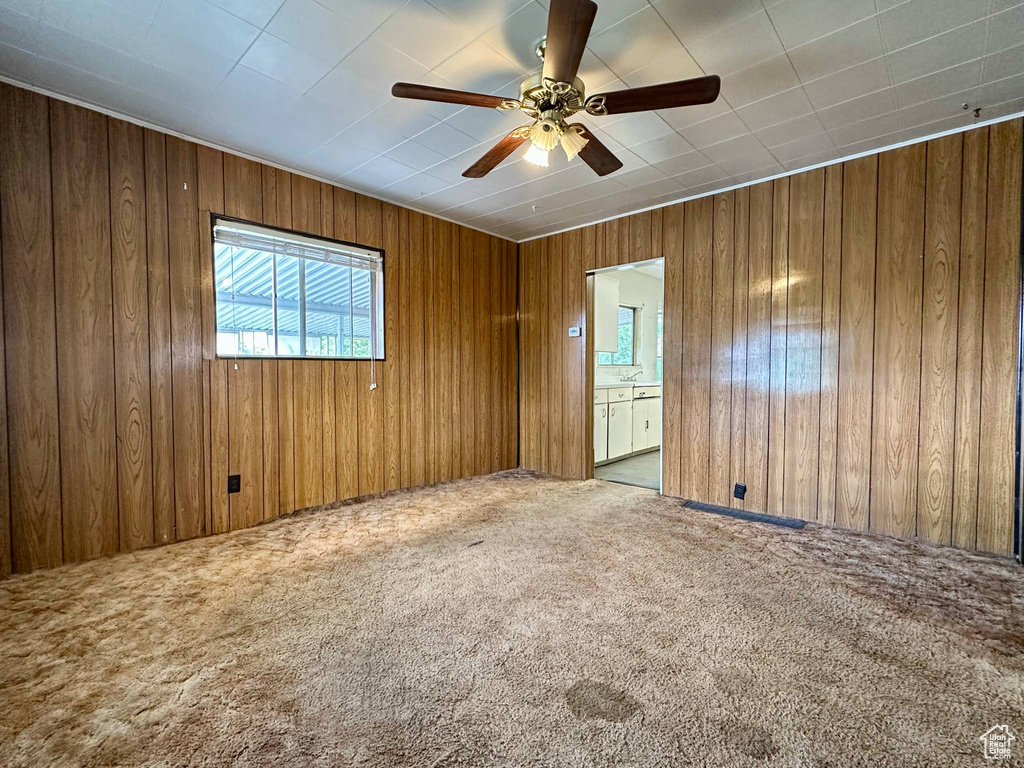 Carpeted spare room with wooden walls and a ceiling fan