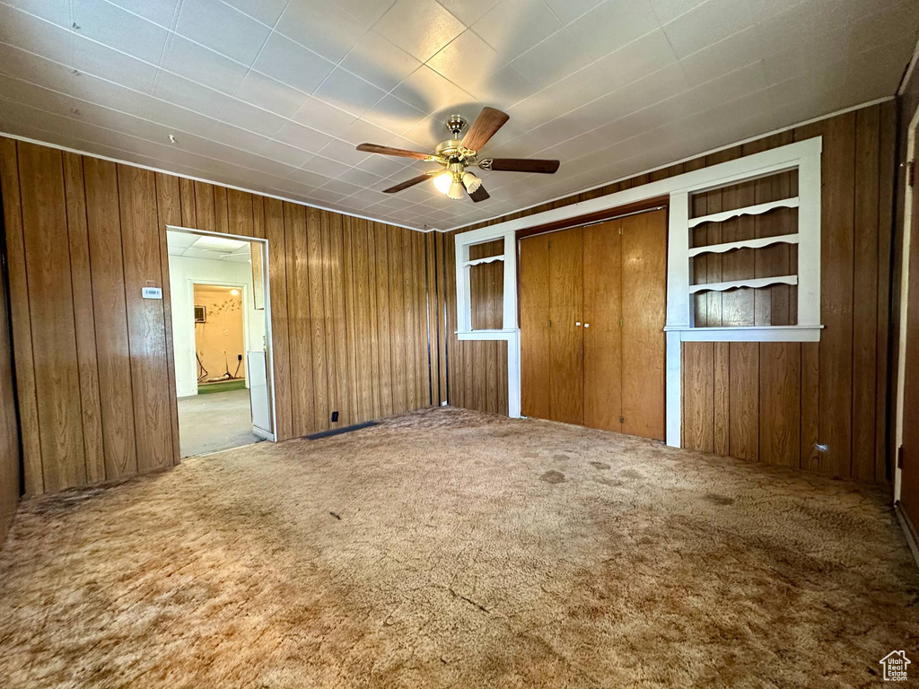 Unfurnished bedroom featuring carpet flooring, wood walls, and a ceiling fan