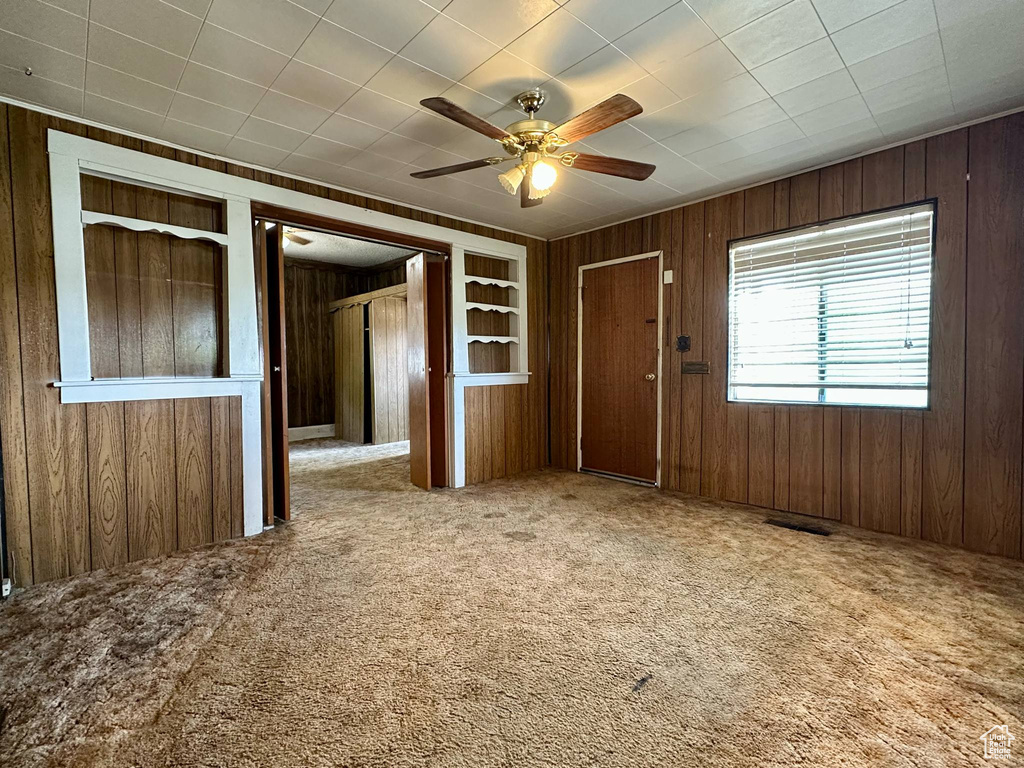 Spare room featuring wooden walls, carpet floors, and ceiling fan
