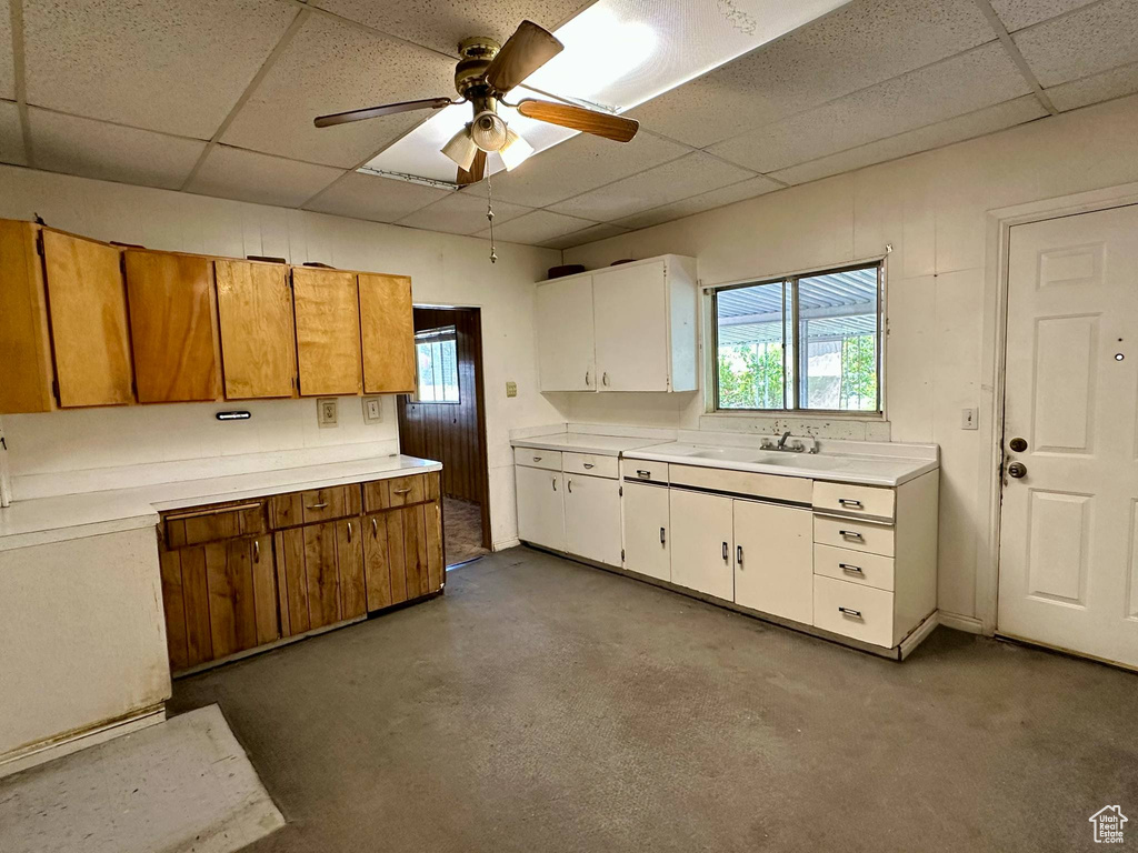 Kitchen with a drop ceiling, light countertops, ceiling fan, brown cabinetry, and white cabinetry