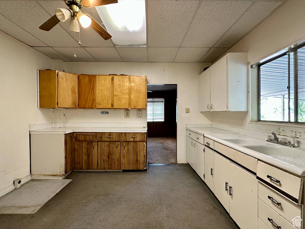 Kitchen featuring a drop ceiling, light countertops, white cabinets, a ceiling fan, and brown cabinetry
