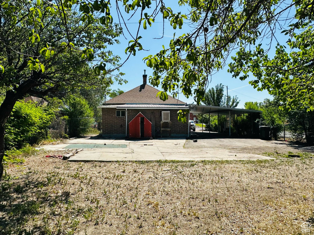 Rear view of property with concrete driveway, an outdoor pool, an attached carport, brick siding, and roof with shingles