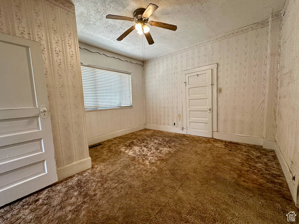 Unfurnished bedroom featuring a textured ceiling, carpet flooring, wallpapered walls, and ceiling fan