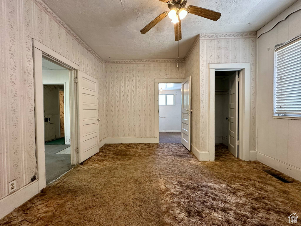 Unfurnished bedroom with a spacious closet, carpet, wallpapered walls, connected bathroom, and a textured ceiling