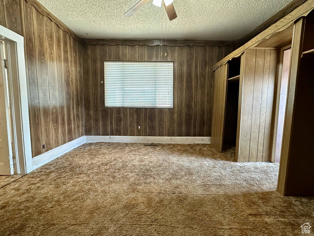 Unfurnished bedroom with carpet floors, a textured ceiling, wooden walls, and ceiling fan