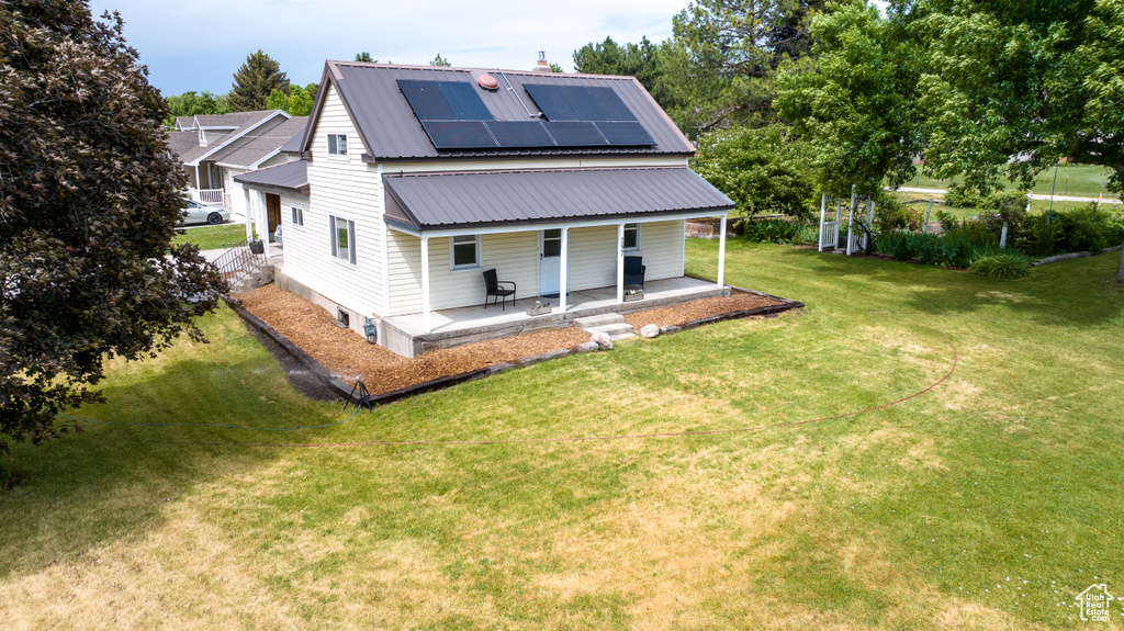 Rear view of house featuring covered porch, roof mounted solar panels, a yard, and a metal roof
