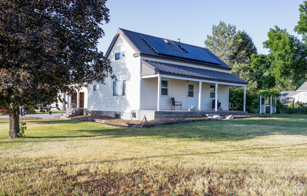 View of front of home with covered porch, solar panels, a front yard, and a metal roof