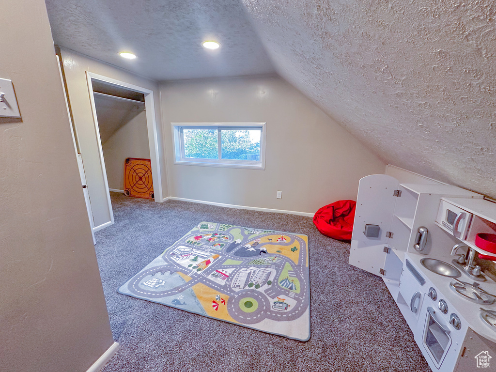 Recreation room with a textured ceiling, carpet floors, and vaulted ceiling