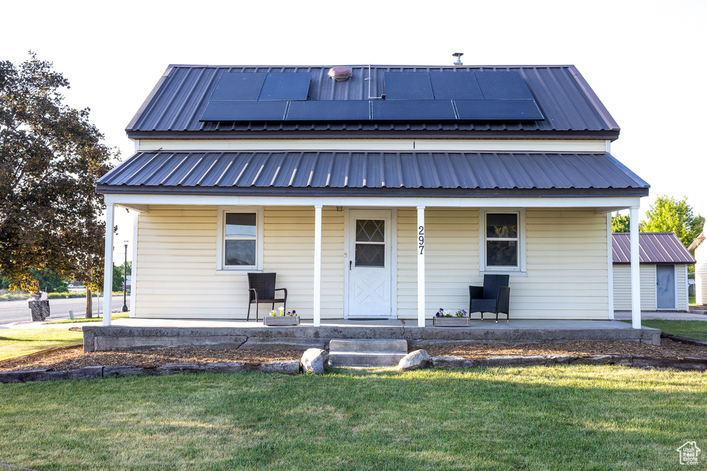 View of front facade featuring a porch, a front yard, a metal roof, and solar panels
