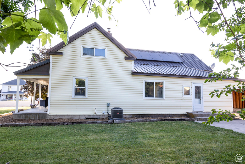 Rear view of property with roof mounted solar panels, a lawn, a metal roof, and a patio