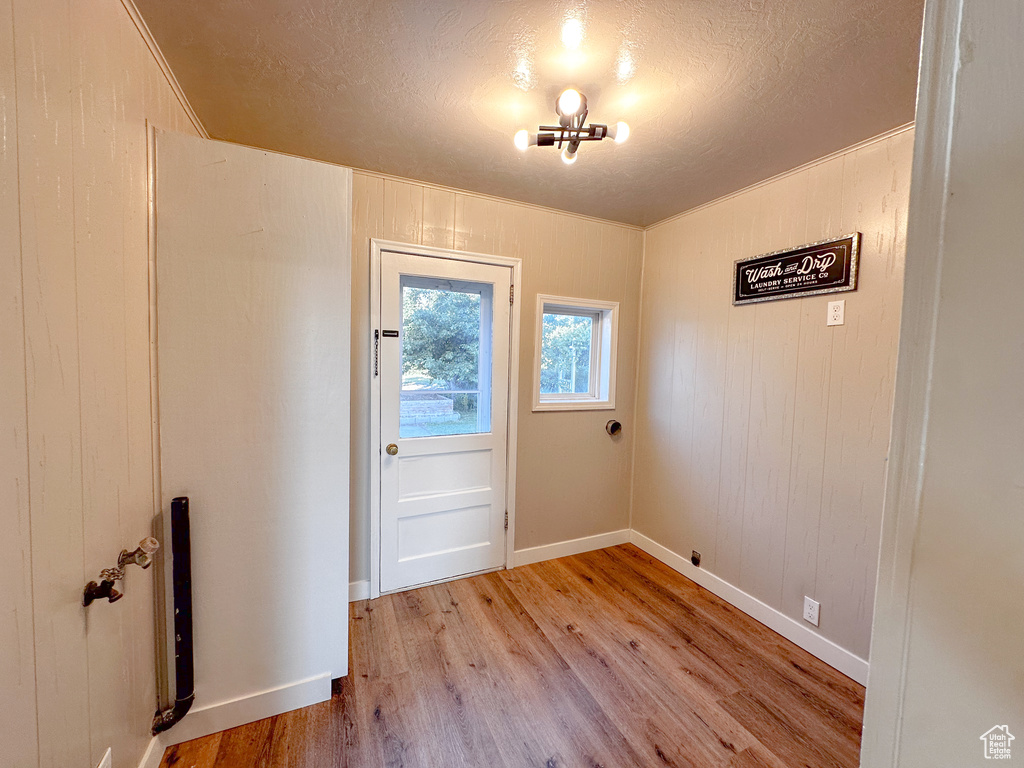 Entryway featuring light wood-style floors, a chandelier, a textured ceiling, wooden walls, and crown molding