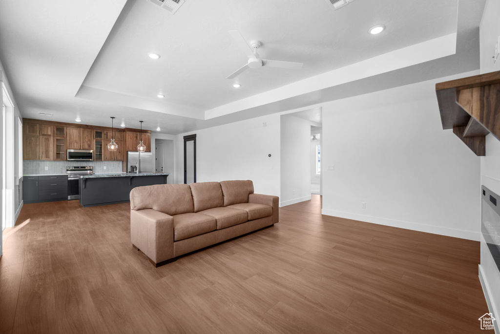 Living room with a raised ceiling, recessed lighting, wood finished floors, and ceiling fan
