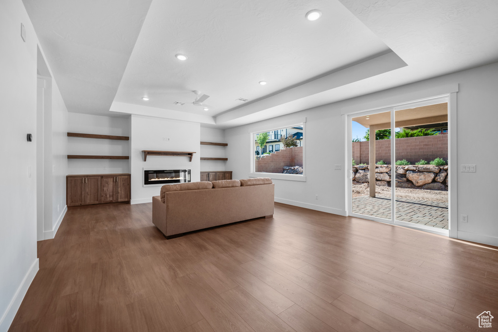 Living room featuring a raised ceiling, a glass covered fireplace, healthy amount of natural light, dark wood-style floors, and recessed lighting