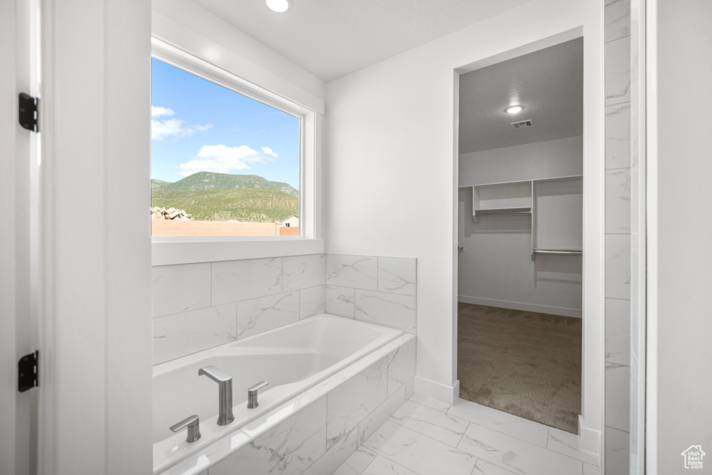 Full bathroom featuring a bath, marble finish flooring, a spacious closet, a mountain view, and recessed lighting