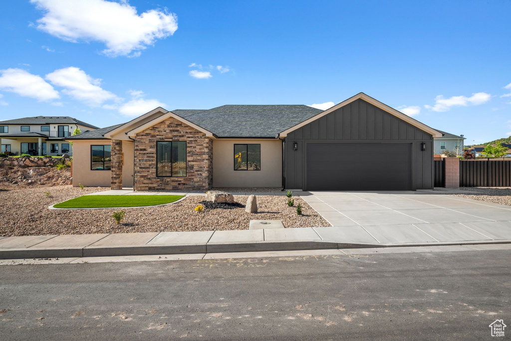 View of front of property with a garage, driveway, board and batten siding, stone siding, and a shingled roof
