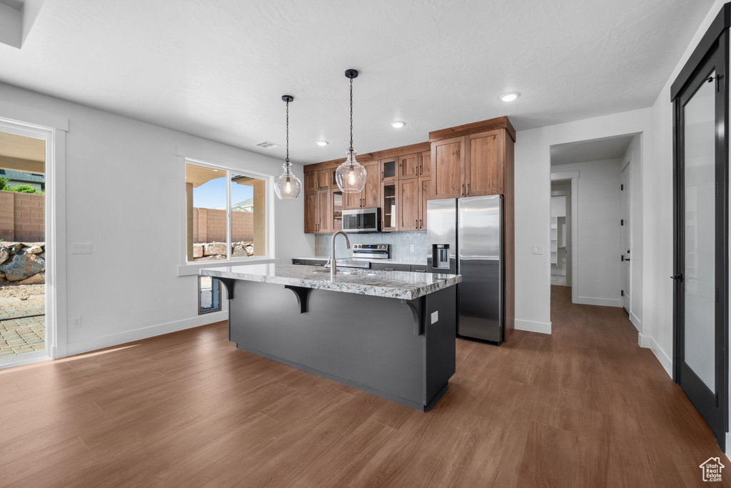 Kitchen featuring appliances with stainless steel finishes, brown cabinetry, a kitchen breakfast bar, dark wood-type flooring, and recessed lighting