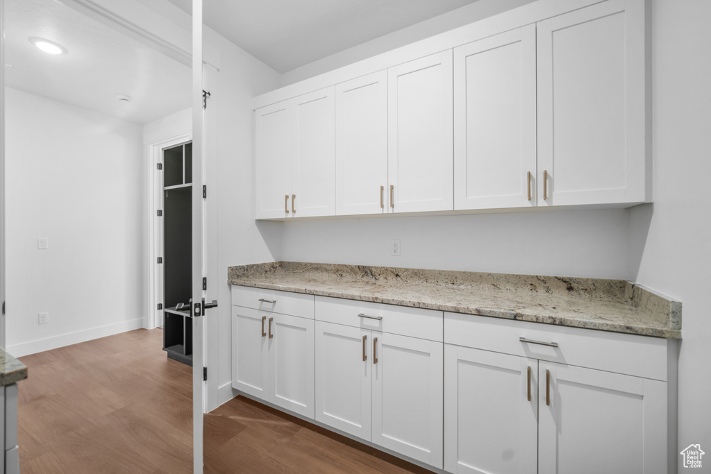 Kitchen featuring wood finished floors, white cabinets, light stone counters, and recessed lighting
