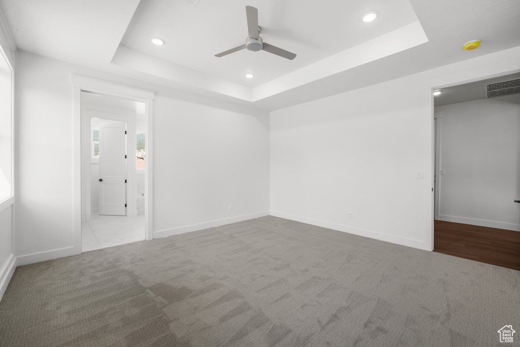 Unfurnished bedroom featuring a raised ceiling, carpet floors, recessed lighting, connected bathroom, and a ceiling fan