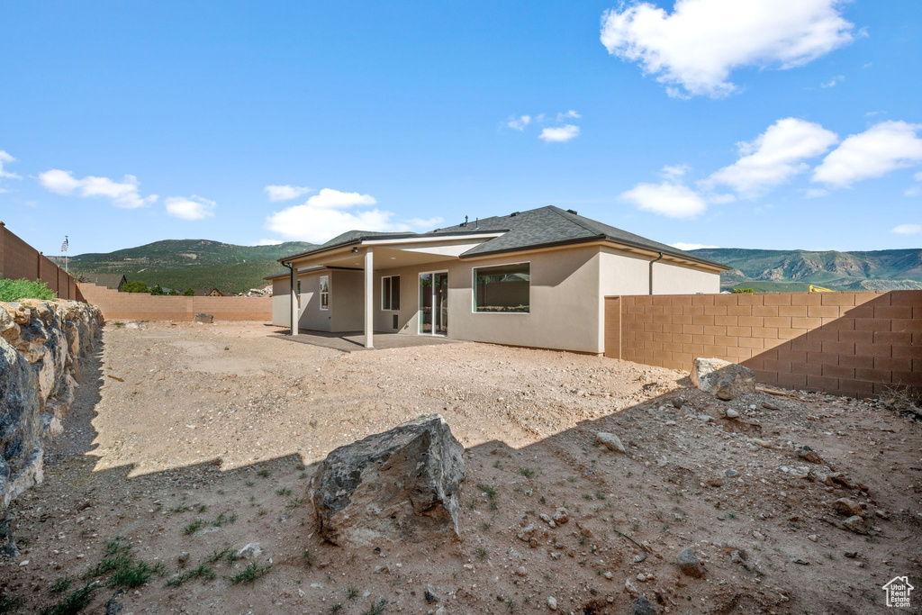 Back of property with a fenced backyard, stucco siding, a mountain view, a patio, and roof with shingles