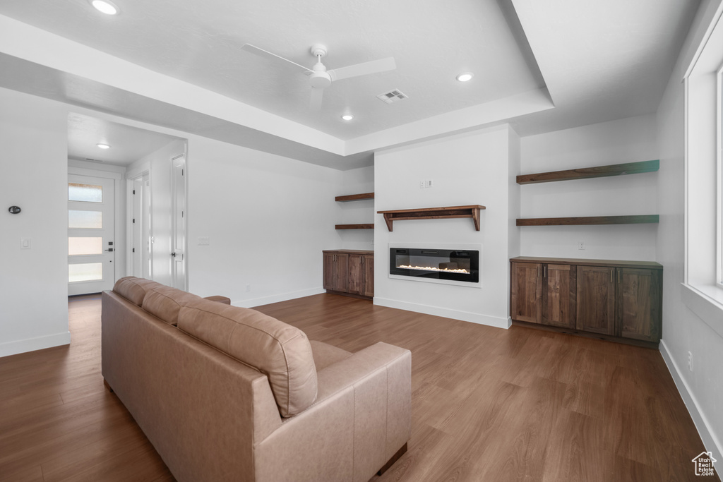 Living room with ceiling fan, wood finished floors, a glass covered fireplace, recessed lighting, and a tray ceiling