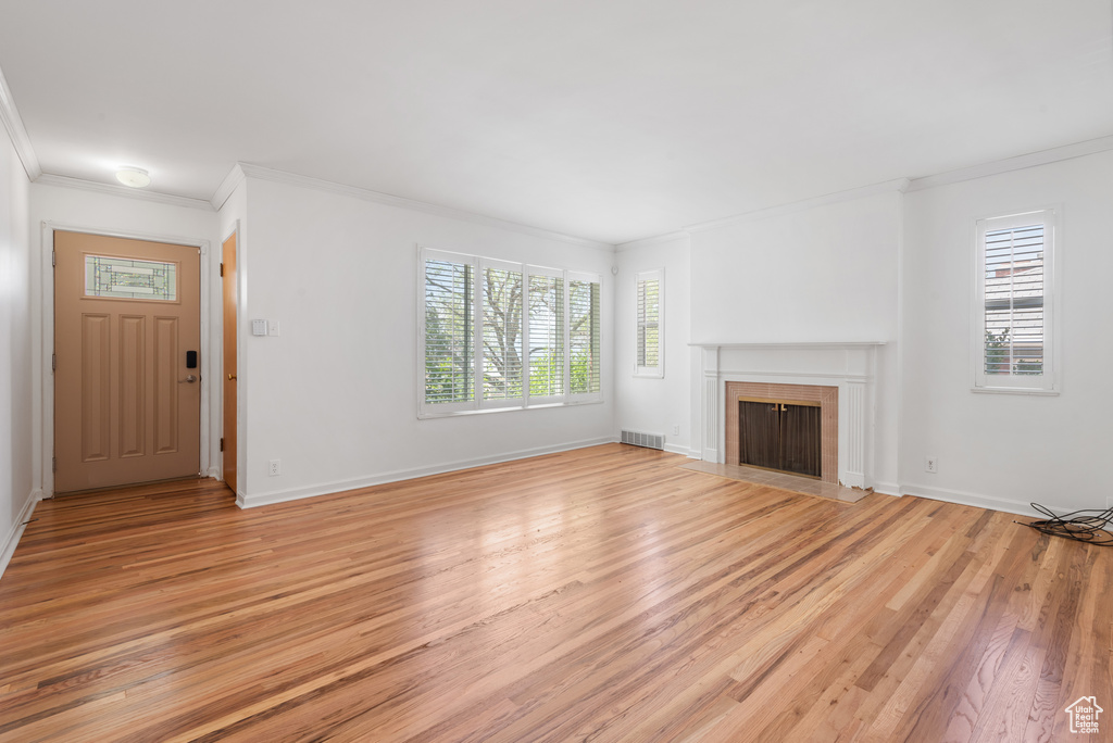 Unfurnished living room with ornamental molding, light wood-type flooring, healthy amount of natural light, and a fireplace