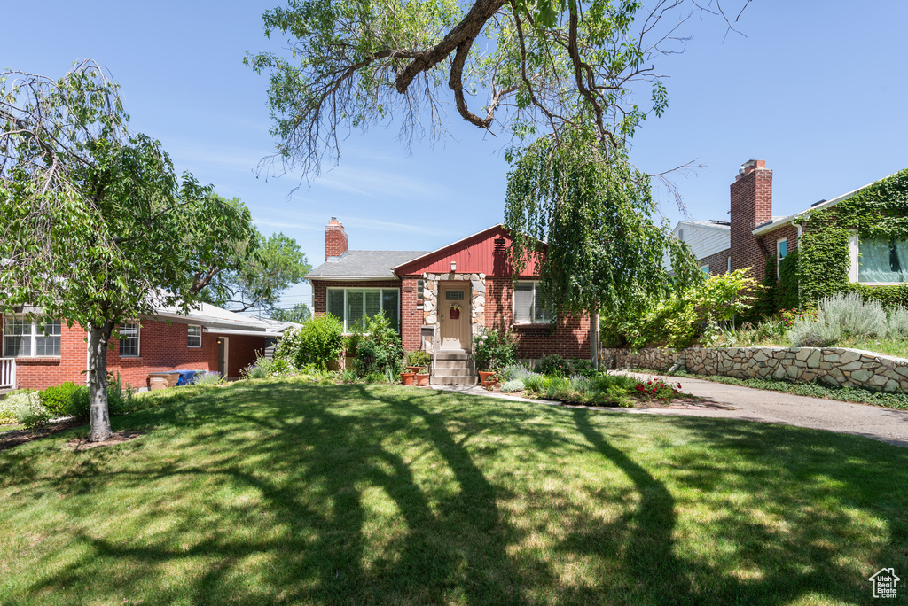 View of front facade featuring brick siding, a front yard, and a chimney