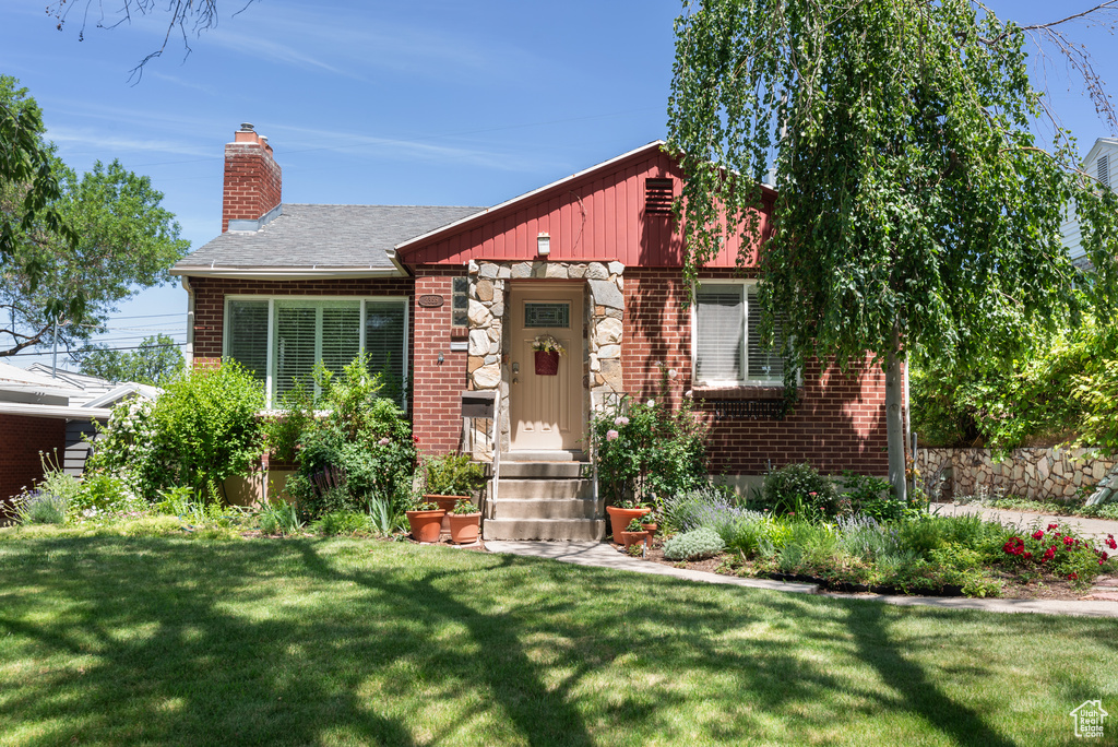 View of front of home with brick siding, a front yard, a chimney, and entry steps