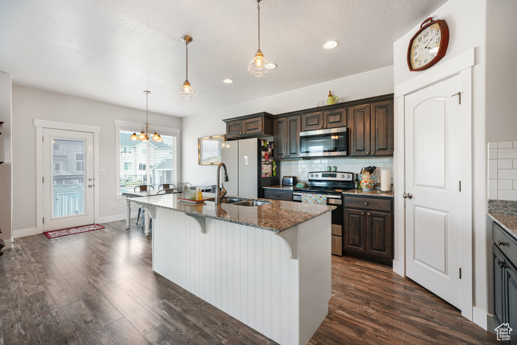 Kitchen featuring appliances with stainless steel finishes, a breakfast bar, dark wood-type flooring, backsplash, and recessed lighting