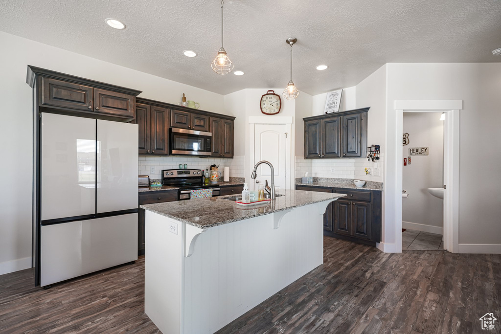 Kitchen featuring appliances with stainless steel finishes, dark stone countertops, a kitchen bar, tasteful backsplash, and dark brown cabinets