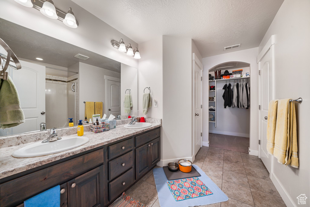 Full bathroom featuring double vanity, a textured ceiling, a spacious closet, a shower, and tile patterned flooring