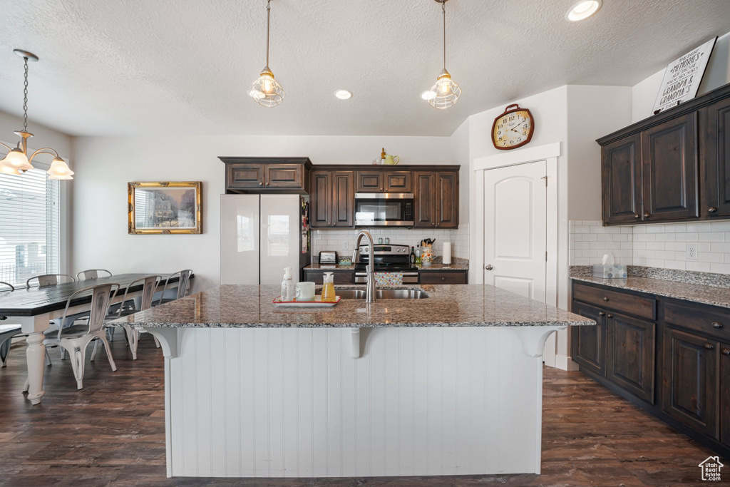 Kitchen featuring stainless steel appliances, a textured ceiling, dark brown cabinets, a kitchen bar, and dark wood-type flooring