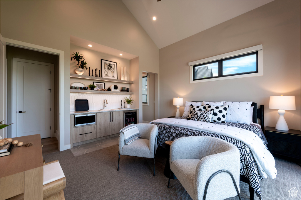 Bedroom featuring beverage cooler, bar with sink, light colored carpet, recessed lighting, and high vaulted ceiling