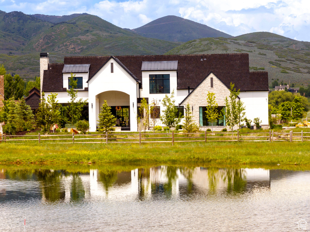 View of front facade with a chimney, stucco siding, stone siding, and a water and mountain view