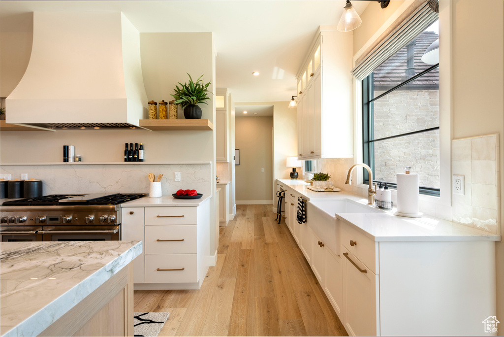 Kitchen with double oven range, custom range hood, light wood-type flooring, white cabinetry, and tasteful backsplash