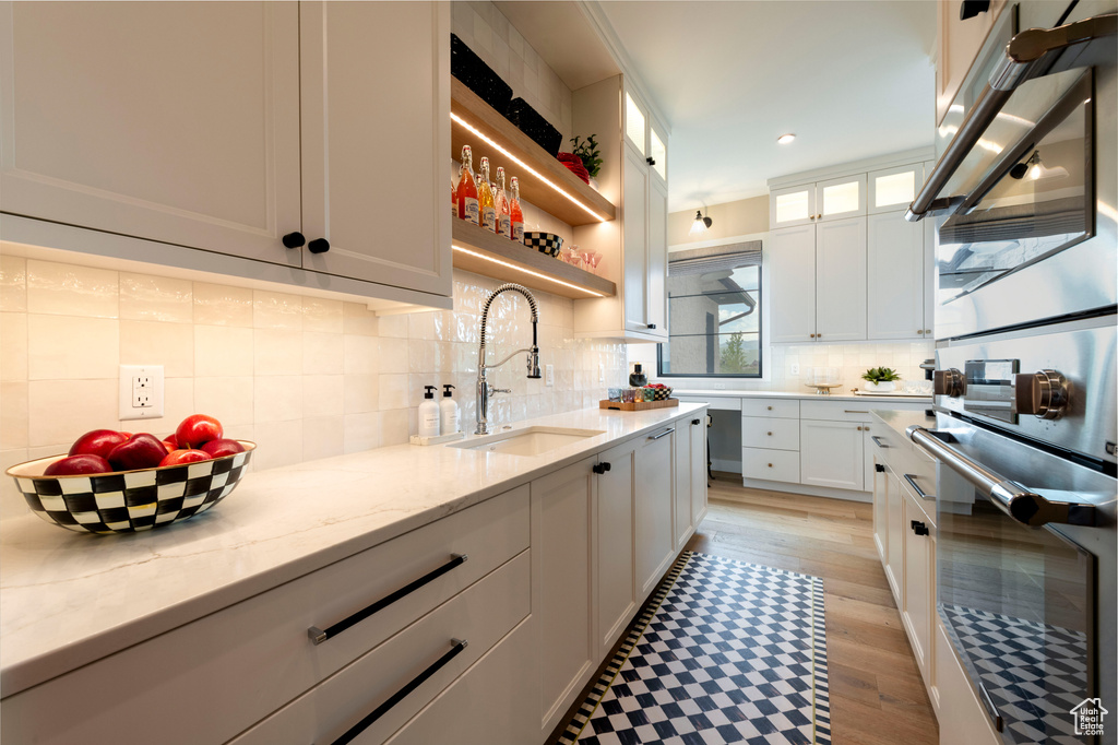 Kitchen with white cabinetry, light stone countertops, stainless steel double oven, tasteful backsplash, and recessed lighting
